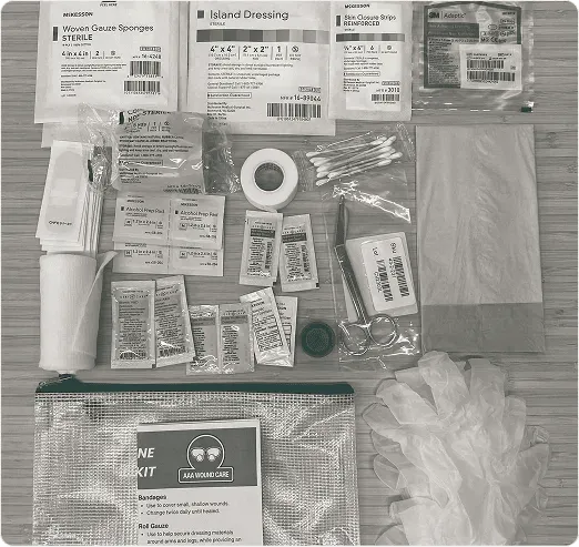 Contents of a wound care kit laid out: gauze sponges, island dressings, ointment packets, roll gauze, tape and an irrigation cap