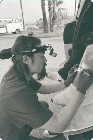 Clinician wearing a headlamp treating a patient's wound outdoors